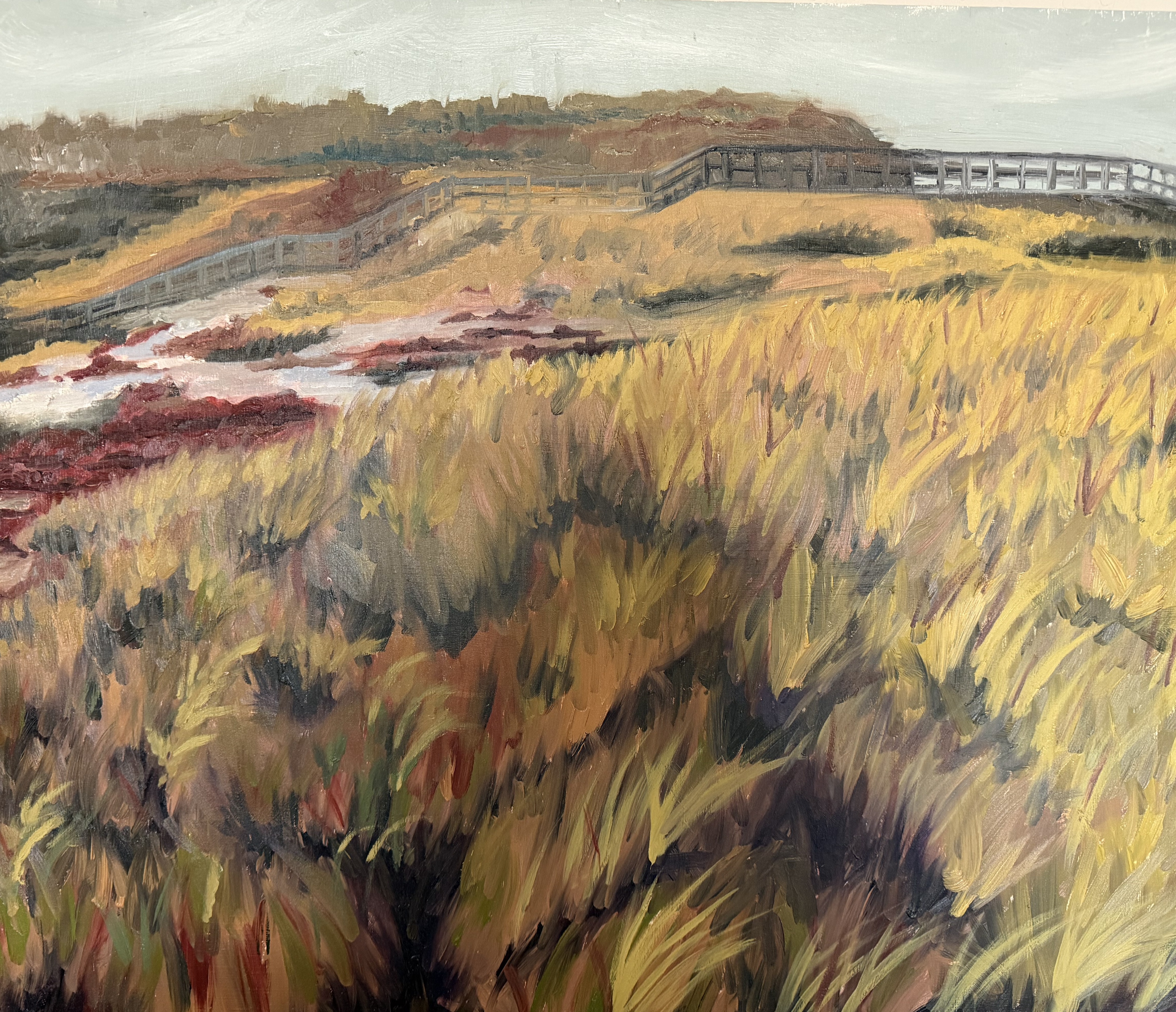 Oil painting of a wooden boardwalk winding through a New England salt marsh — tall golden-yellow and ochre grasses in the foreground, deep red and rust-colored low brush, a glint of tidal water in the middle distance, and a soft sage sky above.