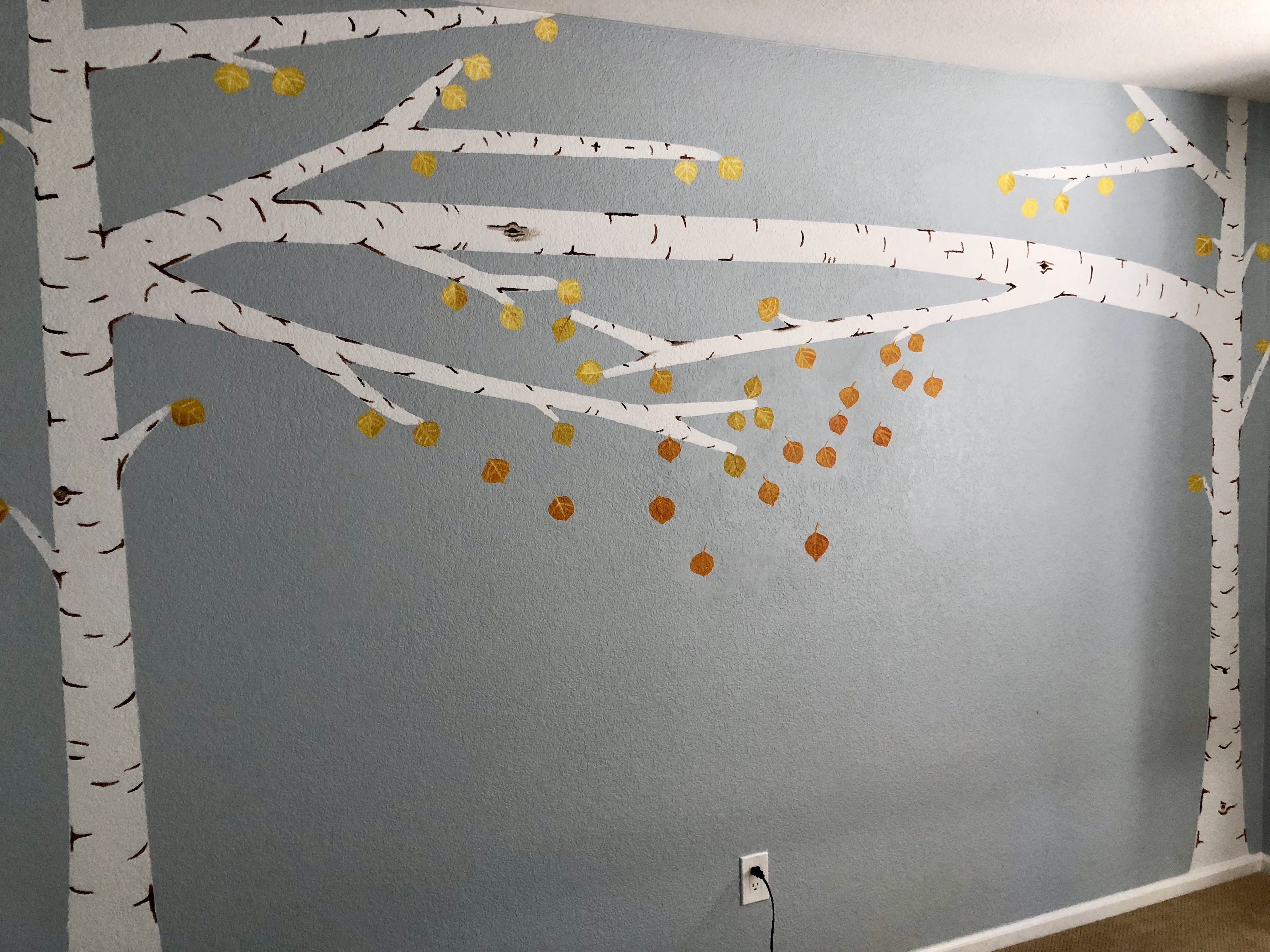 A second daughter's bedroom mural — white aspen trunks with thin branches arcing across a dusty blue wall, hung with hand-painted yellow and orange autumn aspen leaves.