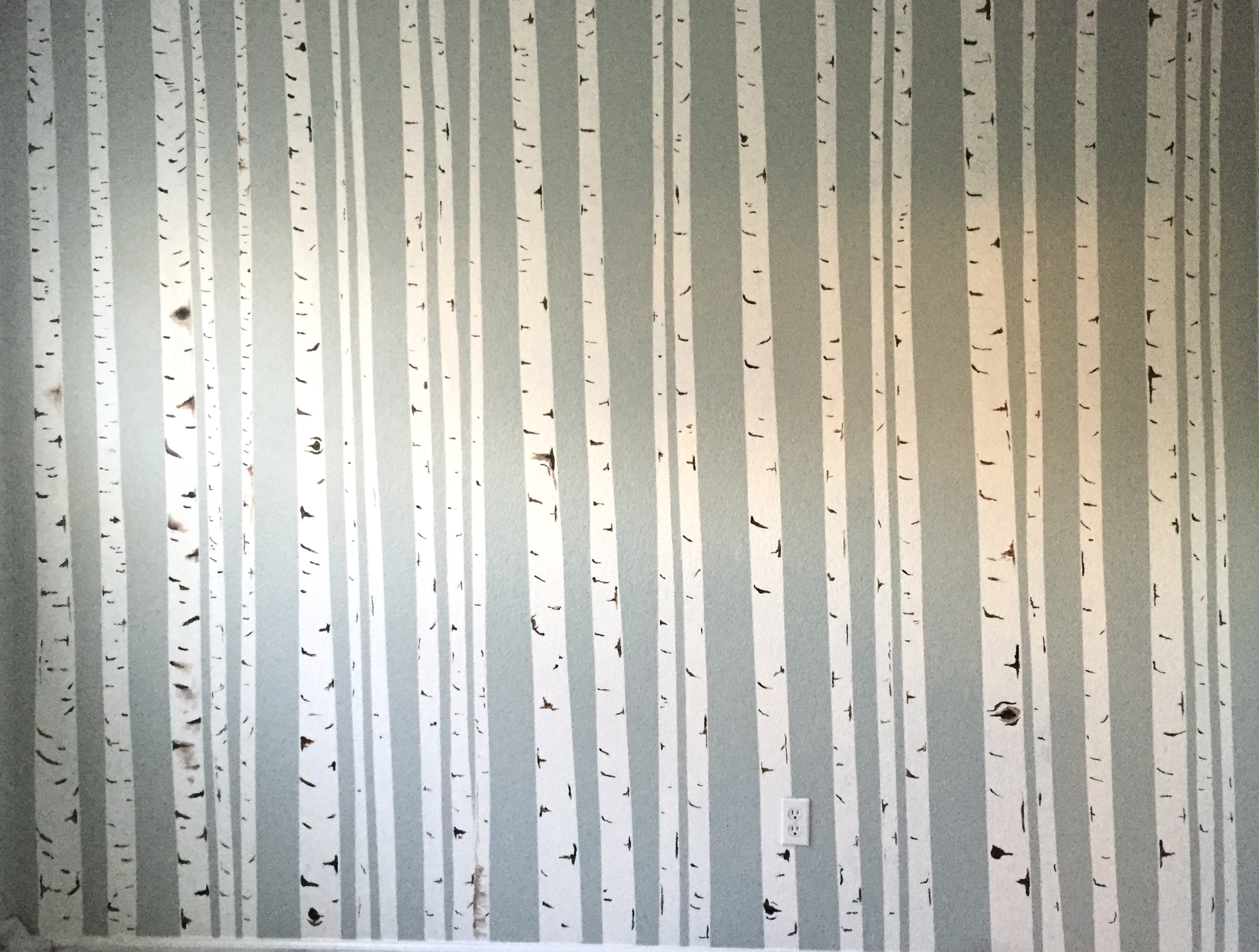 A daughter's bedroom wall painted wall-to-wall with vertical aspen trunks — cream-white trunks marked with dark bark scoring set against a soft sage-blue painted wall.