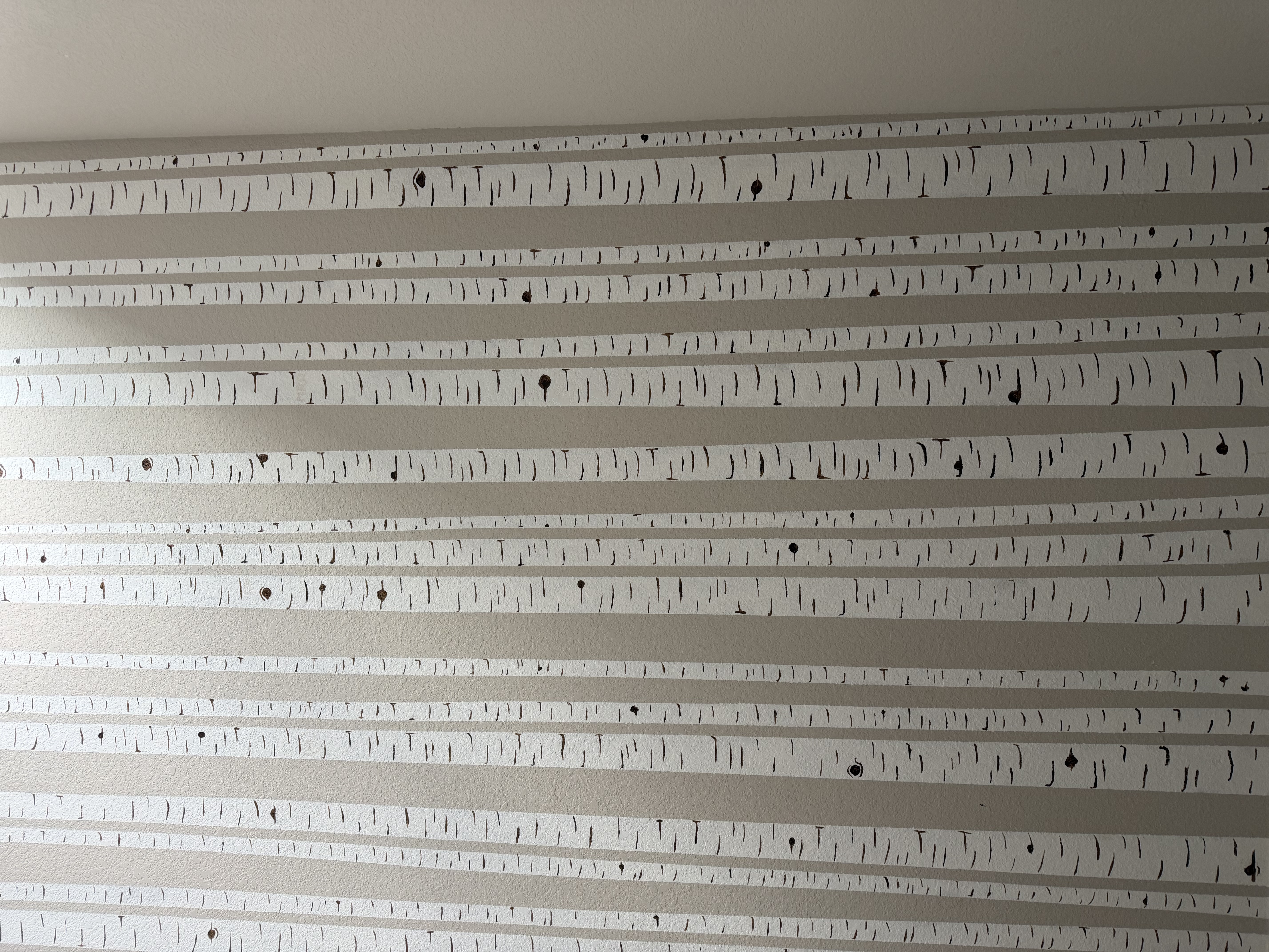 A close-up of the aspen stairwell mural — the cool gray of the existing wall reads as the air between trees, while the white trunks and the fine dark bark scoring are all painted on top.