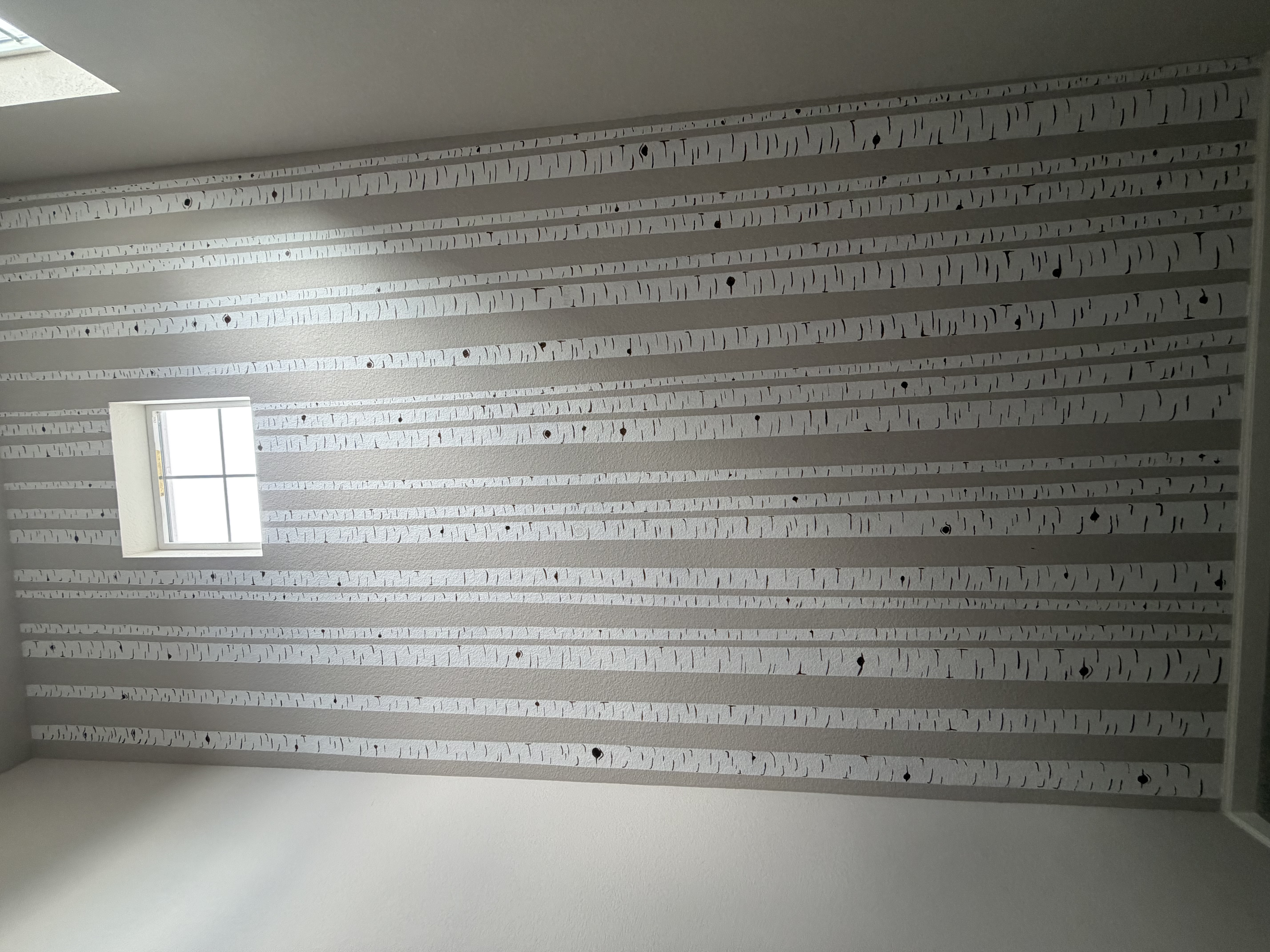 A two-story stairwell wall in our current home painted floor-to-ceiling as an aspen grove — cream-white trunks marked with dark bark scoring rising out of the existing cool-gray wall, with a small square window high near the top.