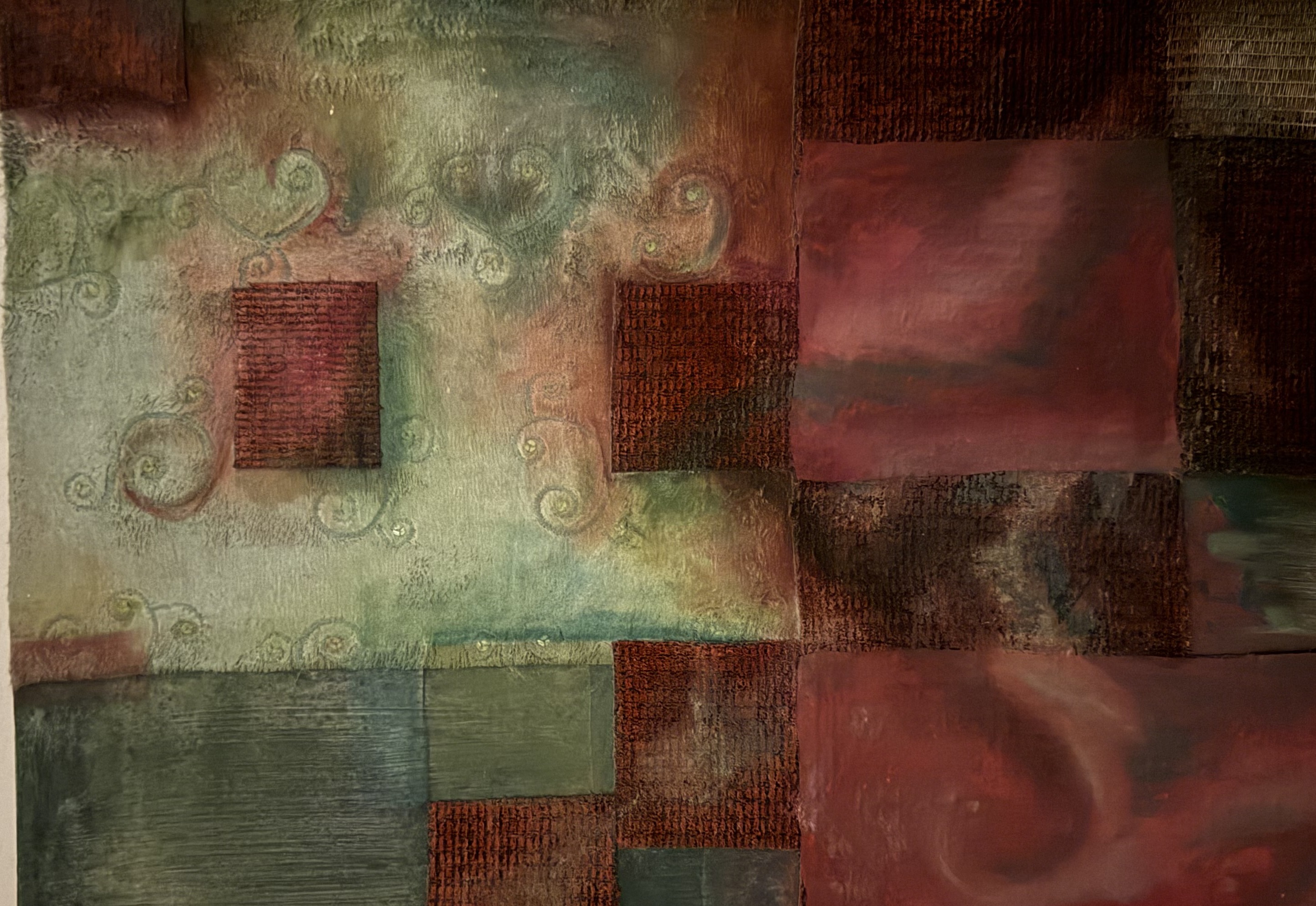 A mixed-media piece of layered rectangles of dyed and painted canvas in deep reds, rust, sage greens, and blues — raw frayed edges, faint scrolling spirals, coarse woven panels and smooth painted cloth.